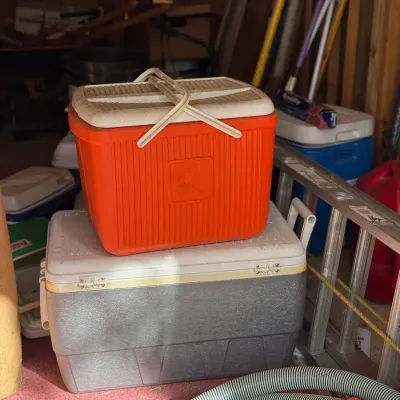 Sale Photo Thumbnail #236: Vintage bright orange insulated cooler chest with a off-white handle and lid, sitting stacked atop a larger textured gray and white cooler.