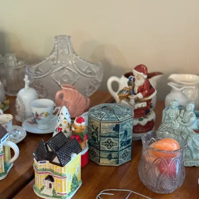 Sale Photo Thumbnail #72: Collection of vintage decorative collectibles, including a miniature house teapot, a Dutch-themed tin, Santa figurines, cut glass vessels, and small china cups.