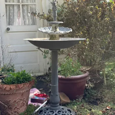 Sale Photo Thumbnail #253: Tiered cast metal garden fountain with a decorative scrollwork base and small figure topper, showing light weathering.