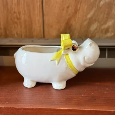 Sale Photo Thumbnail #175: Vintage ceramic hippo planter featuring a glazed white body with an applied yellow bow around its neck.