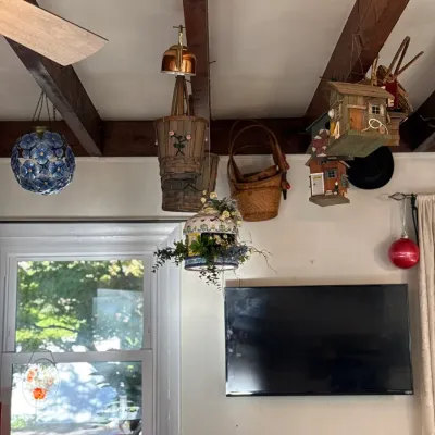 Sale Photo Thumbnail #2: Collection of decorative hanging items including woven baskets, wooden birdhouses, floral orb ornaments, and red glassware displayed on a table below.