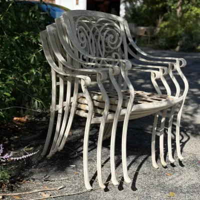 Sale Photo Thumbnail #240: Stack of four white vintage wrought iron patio armchairs with ornate scrollwork backrests.