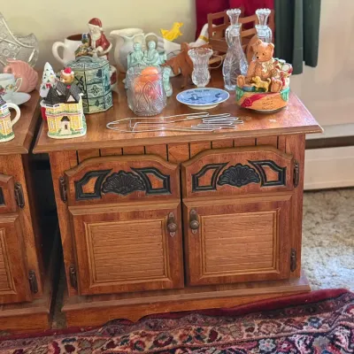 Sale Photo Thumbnail #69: Vintage wooden two-door cabinet featuring detailed paneling, topped with assorted collectibles including glass decanters, figurines, and holiday decor.