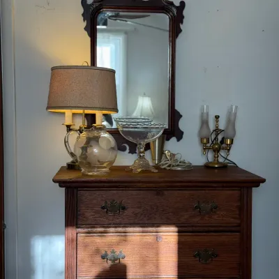 Sale Photo Thumbnail #18: Vintage oak chest of drawers topped with a Chippendale-style wall mirror, table lamp, etched glass pitcher, and brass candelabra.