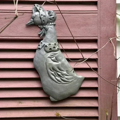Sale Photo Thumbnail #195: Vintage metal goose wall hanging mounted on a pink wooden shutter, featuring a stylized goose in a bonnet and collar.