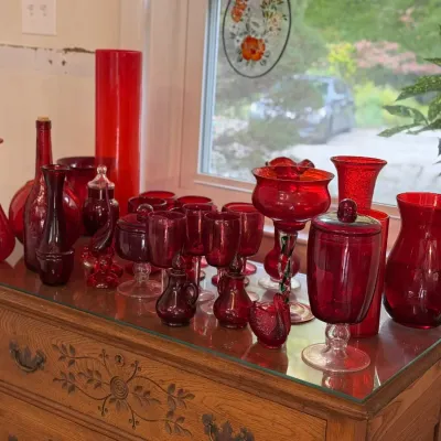 Sale Photo Thumbnail #135: Collection of vintage red and ruby glass items, including vases, stemware, small decanters, and covered jars, displayed on a wooden dresser.