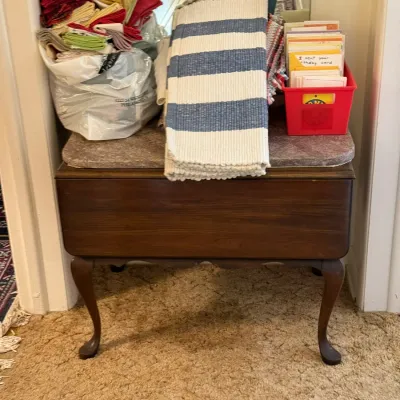 Sale Photo Thumbnail #28: Vintage Queen Anne style wooden bench or table holding a variety of folded textiles, linens, a blue-and-white striped rug, and greeting cards.