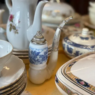 Sale Photo Thumbnail #107: German porcelain smoking pipe with blue transferware scene and silver-tone metal fittings, displayed among vintage tableware.