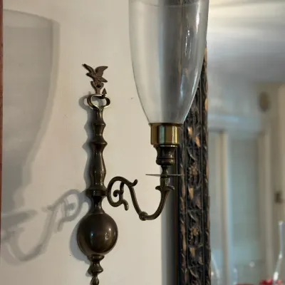 Sale Photo Thumbnail #165: Traditional brass wall sconce featuring an eagle finial, scroll arm, and a clear glass hurricane shade.