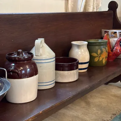 Sale Photo Thumbnail #113: Collection of vintage stoneware crocks, jugs, and pitchers displayed along a dark wood bench.