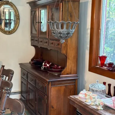 Sale Photo Thumbnail #124: Vintage dark stained wood hutch with glass-door cabinet top, complemented by a suspended metal hanging basket planter and assorted glassware.