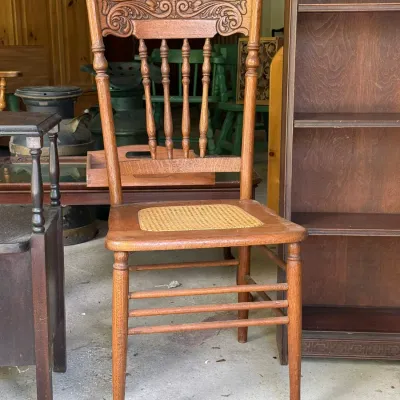 Sale Photo Thumbnail #302: Antique oak dining chair featuring a carved crest rail, spindle backrest, and woven cane seat panel.