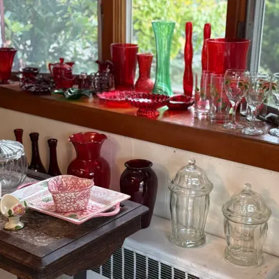 Sale Photo Thumbnail #125: Collection of vintage red and clear glassware, including vases, candy dishes, and floral stemware displayed on a windowsill and wooden side table.