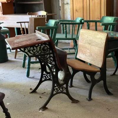Sale Photo Thumbnail #289: Vintage school desks featuring ornate cast iron frames and wooden seats, shown alongside assorted wooden chairs and furniture.