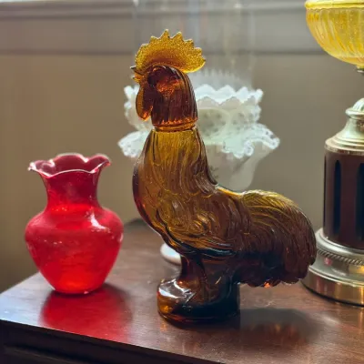 Sale Photo Thumbnail #89: Amber pressed glass rooster bottle, displayed alongside a small ruby red glass vase.