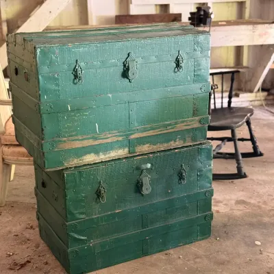 Sale Photo Thumbnail #276: Two stacked antique wooden steamer trunks painted green, featuring metal latches, bands, and corner protectors with age-appropriate wear.