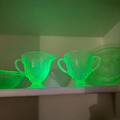 Sale Photo Thumbnail #2: Vintage green uranium glass creamer and sugar bowl set glowing under UV blacklight, featuring intricate Depression glass etchings.