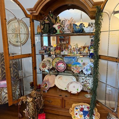 Sale Photo Thumbnail #20: Large wooden curio cabinet with mirrored back and interior lighting, filled with various collectible porcelain pieces, decorative plates, and religious figurines.