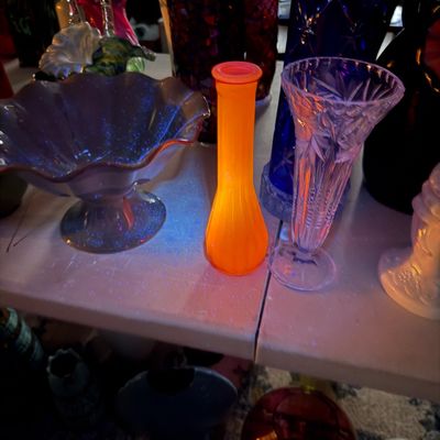 Sale Photo Thumbnail #3: Collection of vintage glass vases and decorative bowls displayed under UV light, featuring a bright orange fluorescent cadmium glass vase.