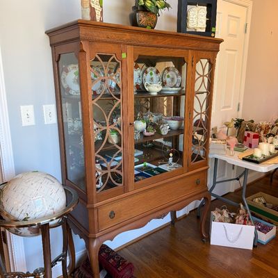 Sale Photo Thumbnail #28: Traditional wooden china cabinet featuring glass doors with decorative fretwork overlays, cabriole legs, and interior shelves filled with porcelain plates and glassware.