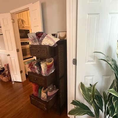 Sale Photo Thumbnail #57: Dark wood storage tower with woven drawer fronts filled with assorted textiles and linens.
