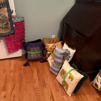 Sale Photo Thumbnail #67: Assortment of decorative throw pillows displayed on a hardwood floor, featuring various patterns, embroidery, and tassel trims, set alongside a mahogany slant-front secretary desk.