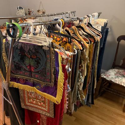 Sale Photo Thumbnail #62: Clothing rack filled with ornate textiles, embroidered pieces, fringed cloths, and various garments.