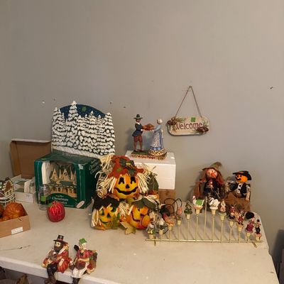 Sale Photo Thumbnail #78: Collection of seasonal holiday decor on a folding table, including Thanksgiving pilgrim figurines, stacked jack-o'-lantern pumpkins, scarecrow dolls, and a brass candle rack.