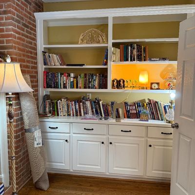 Sale Photo Thumbnail #31: Large white custom built-in bookcase and storage cabinet unit filled with assorted books and decorative items, alongside a rolled area rug and floor lamp.