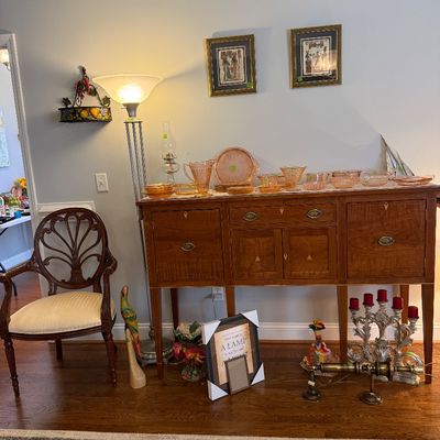 Sale Photo Thumbnail #27: Traditional wooden sideboard displaying an array of vintage pink depression glass, alongside a carved armchair, floor lamp, and framed wall art.