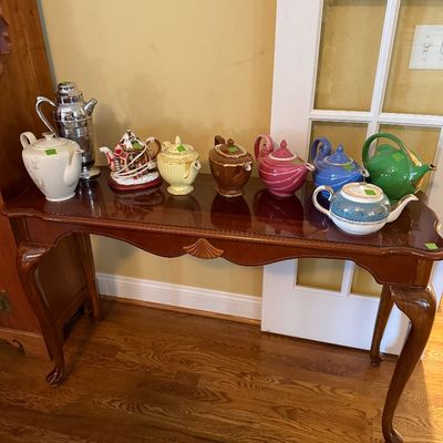 Sale Photo Thumbnail #39: A collection of vintage teapots and a chrome cocktail shaker arranged on a Queen Anne style wooden sofa table with carved shell details.