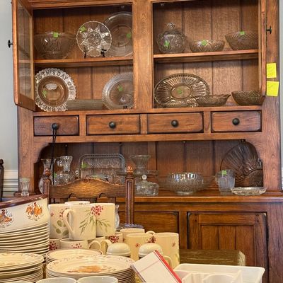 Sale Photo Thumbnail #16: Large wooden hutch filled with clear and colored pressed glassware, displayed above a dining table laden with ceramic dishware.