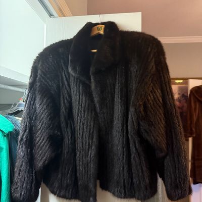 Sale Photo Thumbnail #77: Dark brown or black mink fur jacket featuring a wide collar and relaxed silhouette, displayed on a wooden hanger.
