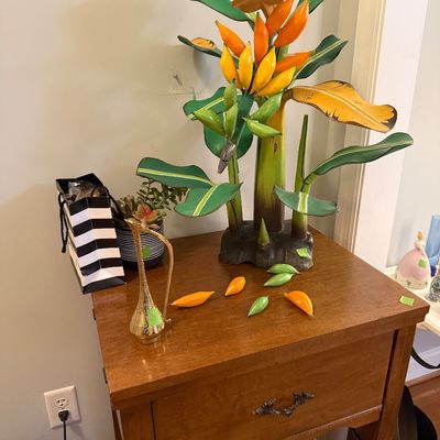 Sale Photo Thumbnail #46: Painted metal banana tree sculpture with detachable fruits, sitting atop a wooden single-drawer nightstand alongside a small brass pitcher.