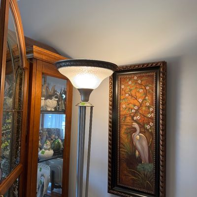 Sale Photo Thumbnail #19: Modern torchiere floor lamp with a brushed metal multi-rod stem and a textured glass shade, shown next to a framed heron oil painting.