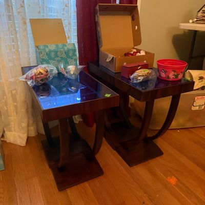 Sale Photo Thumbnail #64: Pair of modern dark wood end tables with curved legs and glass tops, displaying various boxed Christmas ornaments and holiday decorations.