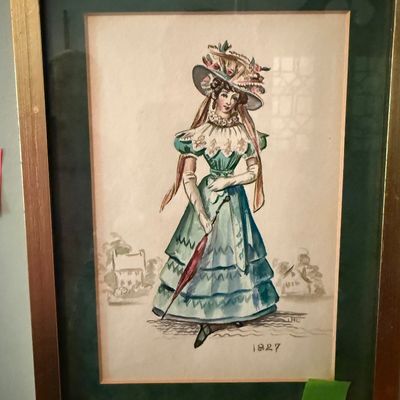 Sale Photo Thumbnail #50: Framed fashion illustration print depicting a woman in 1827 attire, mounted in a dark green mat with a gold-tone wooden frame.