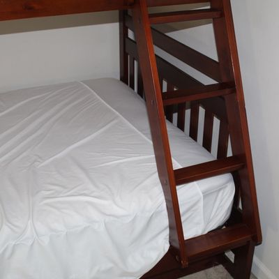 Sale Photo Thumbnail #80: Solid wood wooden bunk bed frame in a rich cherry finish with an integrated ladder and fitted white sheet.