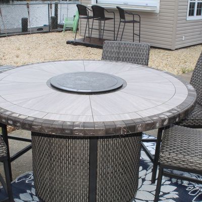 Sale Photo Thumbnail #50: Outdoor patio set featuring a round fire pit table with a tile top and woven resin wicker base, accompanied by matching high-back armless chairs.