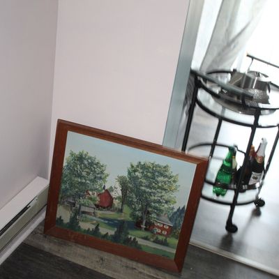 Sale Photo Thumbnail #19: Framed original oil painting depicting a rural landscape with red barns, resting on the floor beside a black metal bar cart.
