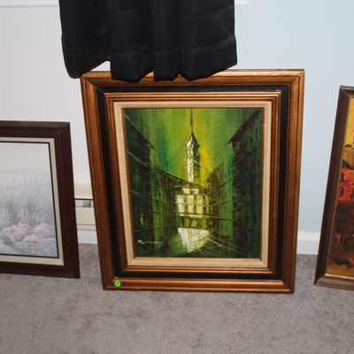 Sale Photo Thumbnail #73: Trio of mid-century framed oil paintings, featuring a vibrant green city street scene in an ornate wood frame alongside a coastal landscape and a European village scene.