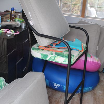 Sale Photo Thumbnail #63: Outdoor patio bar stool with black metal frame, palm-patterned cushion, and grey backrest, surrounded by pool floats, cushions, and beach gear.