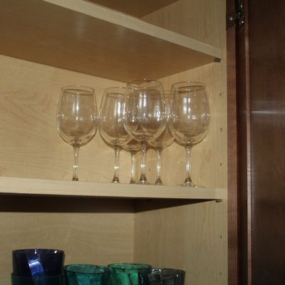 Sale Photo Thumbnail #2: Set of clear glass stemmed wine glasses stored on a wooden cabinet shelf alongside colored glass drinkware.