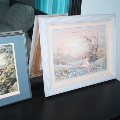 Sale Photo Thumbnail #83: Two framed art prints resting on a dark dresser, including an impressionistic landscape with a figure in a pink gown and a watercolor depicting the Golden Gate Bridge.