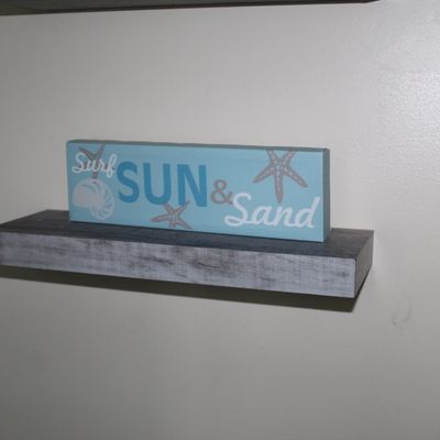 Sale Photo Thumbnail #93: Coastal-themed "Surf, Sun & Sand" decorative box sign resting on a wall-mounted weathered grey floating shelf.
