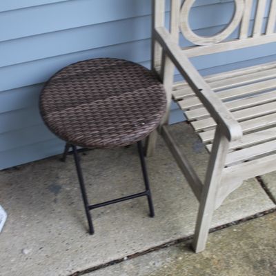 Sale Photo Thumbnail #42: Small round woven wicker top folding side table with a black metal frame, set outdoors near a bench.
