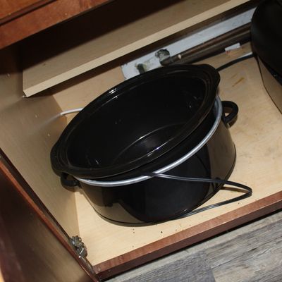 Sale Photo Thumbnail #5: Black oval slow cooker with removable ceramic insert, stored inside a wooden lower cabinet alongside an air fryer.