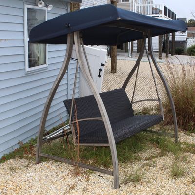 Sale Photo Thumbnail #57: Outdoor patio swing with a dark wicker bench seat, metal arched frame, and dark blue fabric canopy top.