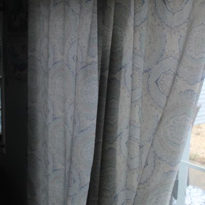Sale Photo Thumbnail #27: Pair of full-length window drapes featuring a soft blue and beige mandala or medallion print fabric, hung beside a glass door.