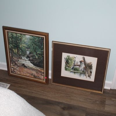 Sale Photo Thumbnail #91: Two framed wall art pieces leaning against a wall, including an oil painting of a forest waterfall and a matted architectural print or watercolor.